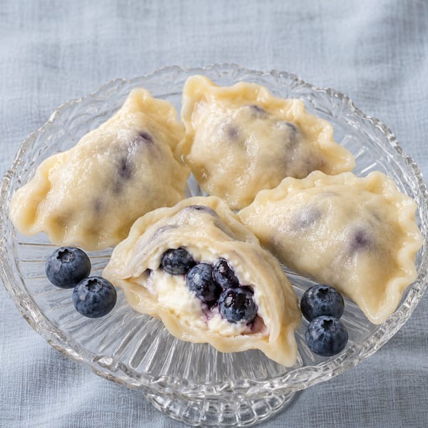 Pierogi Borówkowa Chmurka na szklanej paterze; w rozciętym pierogu mascarpone z borówkami, obok świeże borówki