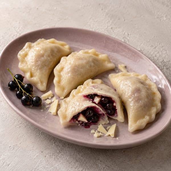 Pierogi fantazyjne na liliowym półmisku; w rozciętym pierogu czarna porzeczka i biała czekolada, obok gałązka porzeczek
