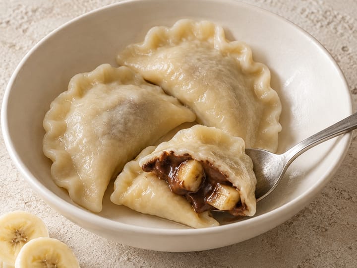 Pierogi z bananem i czekoladą w białej misce; rozcięty pieróg pokazuje plasterki banana w czekoladzie