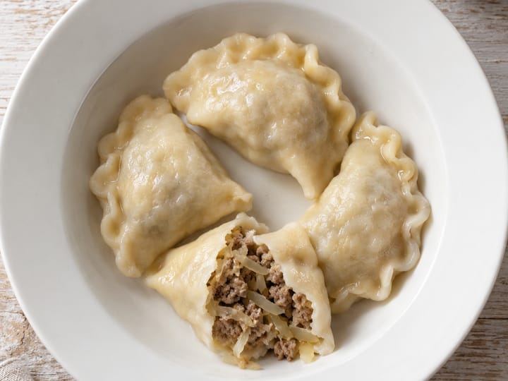 Pierogi z kapustą i mięsem na białym głębokim talerzu; w rozciętym pierogu mielone mięso z kapustą