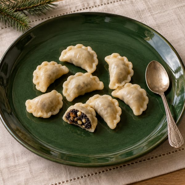 Małe pierożki wigilijne na ciemnozielonym talerzu; rozcięty pierożek pokazuje farsz makowy z bakaliami, obok gałązka świerku